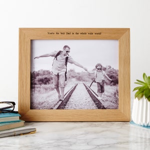 May include: A light oak picture frame holding a monochrome photograph of a man and child walking on railway tracks. The frame includes the text: "You're the best Dad in the whole wide world!"