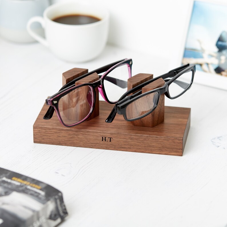 May include: A wooden glasses holder with two pairs of glasses resting on it. The holder is engraved with the initials "H.T."
