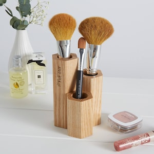 May include: Wooden makeup brush holder with three compartments. The holder is engraved with the text "#NotFilter". There are three brushes in the holder, two large fluffy brushes and one smaller brush.