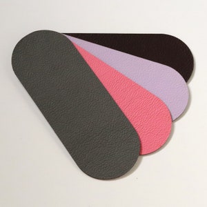 K&ouml;nnte beinhalten: Vier Lederst&uuml;cke in F&auml;cheranordnung. Die Farben sind Dunkelgrau, Rosa, Lavendel und Dunkelbraun. Jedes St&uuml;ck hat ein abgerundetes Ende und eine strukturierte Oberfl&auml;che, was auf ein Lederprodukt hindeutet.