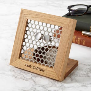 Könnte beinhalten: Holz-Manschettenknöpfe-Display mit einer Metallgitterfront, die silberne Manschettenknöpfe hält. Auf dem Etui steht "Dad's Cufflinks". Die Manschettenknöpfe sind rund und haben ein gebürstetes Metall-Finish. Das Etui steht auf einer Marmoroberfläche.