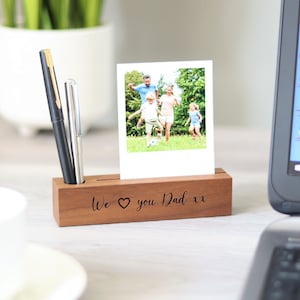 Könnte beinhalten: Ein Holz-Schreibtisch-Organizer mit einem Foto und zwei Stiften. Das Foto zeigt eine Familie beim Spielen im Freien. Der Organizer hat den Text "We love you Dad xx" auf der Vorderseite eingraviert.