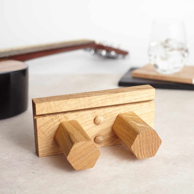 May include: A wooden wall-mounted guitar hook with two hexagonal knobs. The hook is made of light brown wood and has a natural finish.