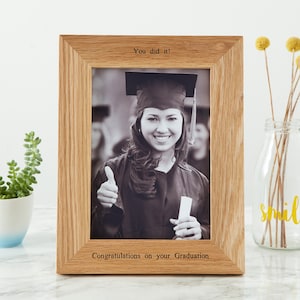 Könnte beinhalten: Ein Holzfotorahmen mit einem Abschlussfoto. Der Rahmen trägt oben den Text "You did it!" und unten "Congratulations on your Graduation". Das Foto zeigt eine Person in einem Abschlusskleid.