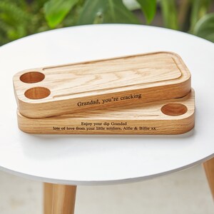 May include: Two wooden serving trays with a personalized message. The top tray has two small holes for dipping. The message reads "Grandad, you're cracking. Enjoy your dip Grandad. Lots of love from your little soldiers, Alfie & Billie xx".