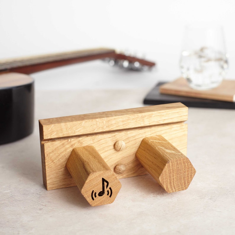 May include: Wooden headphone stand with two hexagonal-shaped holders. The stand has a groove and two small holes. One holder has a carved musical note with sound waves.