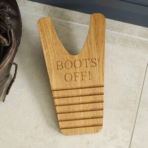 Pu&ograve; includere: Un cavastivali in legno chiaro, inciso con le parole "BOOTS OFF!". Il cavastivali ha una forma a V e scanalature orizzontali. Uno stivale in pelle marrone &egrave; parzialmente visibile a sinistra. Lo strumento &egrave; progettato per togliere gli stivali.