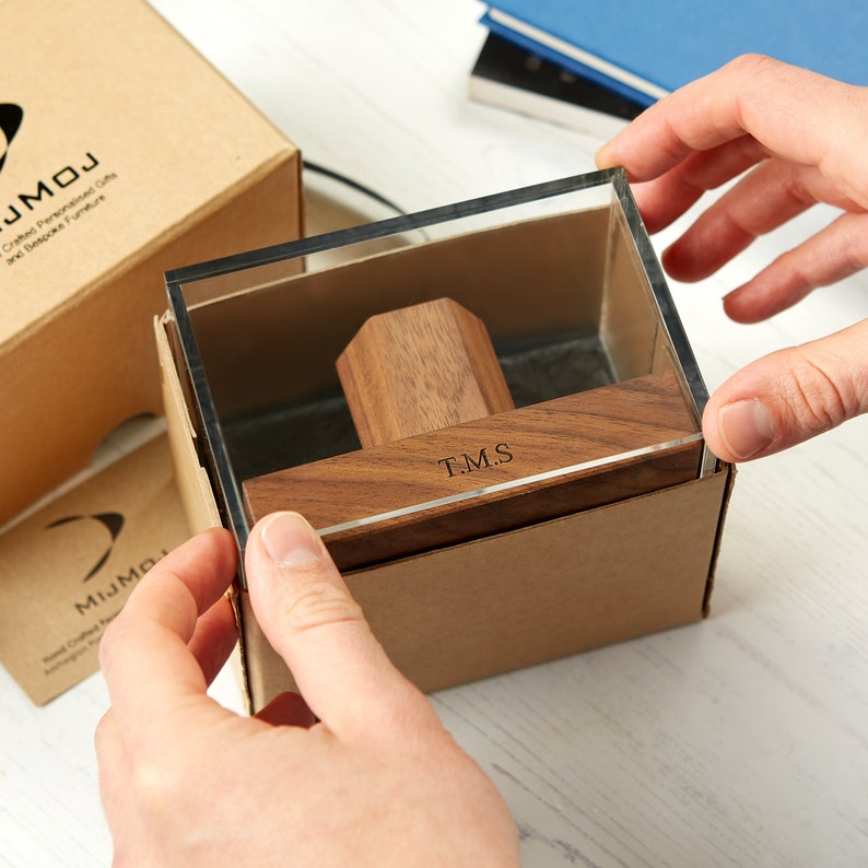 May include: A wooden display box with a clear acrylic lid, displaying a personalized wooden item. The item has the initials "T.M.S." engraved on it. The box is in a cardboard container, suggesting a gift or presentation item.