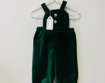 Könnte beinhalten: Ein dunkelgrüner Samt-Baby-Overall mit einem weißen Etikett, auf dem "Babyboutique" steht. Der Overall hat zwei grüne Knöpfe.