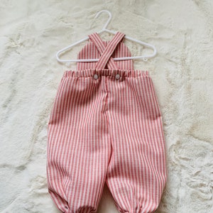 K&ouml;nnte beinhalten: Rot-wei&szlig; gestreifter Baby-Overall mit Kreuzriemen-Design und Knopfverschluss.