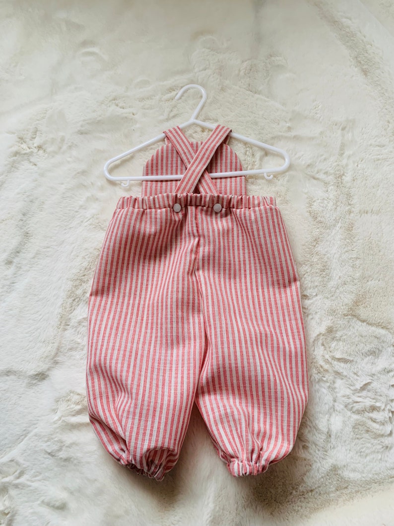 K&ouml;nnte beinhalten: Rot-wei&szlig; gestreifter Baby-Overall mit Kreuzriemen-Design und Knopfverschluss.