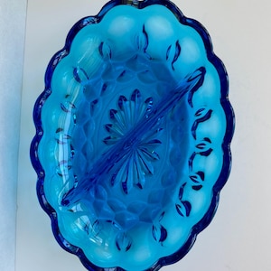 May include: An oval serving dish in shades of blue, divided into two sections. It has a scalloped edge and a central divider. The interior features a textured pattern and leaf-like accents. A vintage piece for serving snacks or appetizers.