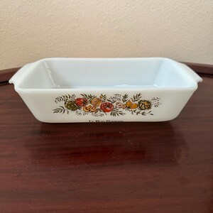 May include: White rectangular baking dish with a colorful floral and vegetable design. The dish has a slightly flared shape with small handles on each side. The design includes images of tomatoes, corn, and other produce.