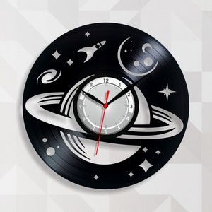 Può includere: Un orologio in vinile nero con un quadrante bianco e lancette nere. Il quadrante presenta un design con un pianeta con anelli, un razzo e stelle. L'orologio ha un diametro di 30,5 cm.