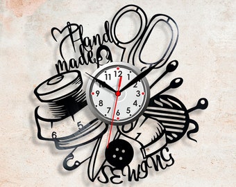 May include: A black and white vinyl record clock with a sewing theme. The clock face is silver with black numbers and hands. The design includes scissors, thread, buttons, and the words "Hand Made Sewing".