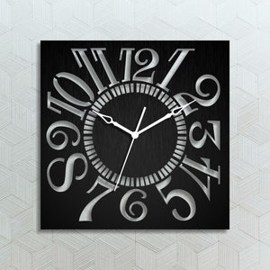 Könnte beinhalten: Eine schwarze quadratische Uhr mit silbernen Zahlen und Zeigern. Die Zahlen sind in einem Kreis um das Zifferblatt angeordnet, wobei die 12 oben und die 6 unten sind. Die Zeiger zeigen auf die 10 und die 2.