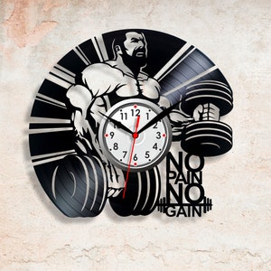 May include: Black vinyl record clock featuring a silhouette of a bodybuilder lifting weights. The clock face is white with black numbers and hands. The text "NO PAIN NO GAIN" is printed below the clock face.