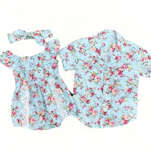 Puede incluir: Conjunto de ropa con estampado floral azul claro. Incluye un pelele con hombros descubiertos, una diadema y una camisa de manga corta. Las flores son rosas y rojas.