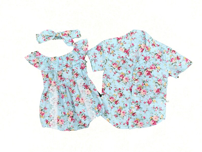 Puede incluir: Conjunto de ropa con estampado floral azul claro. Incluye un pelele con hombros descubiertos, una diadema y una camisa de manga corta. Las flores son rosas y rojas.