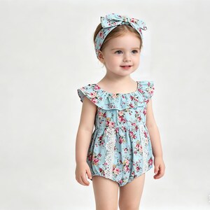 Puede incluir: Una ni&ntilde;a peque&ntilde;a con un pelele azul claro y una diadema a juego, ambos adornados con un estampado floral de rosas rosas y rojas. El pelele presenta un escote con volantes y ribete de encaje blanco.