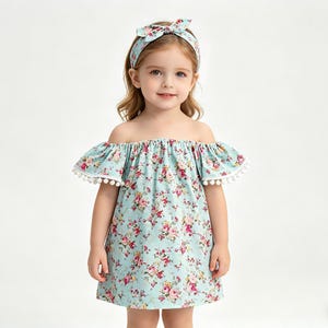 Puede incluir: Un vestido azul claro con hombros descubiertos con un estampado floral y ribete de pomp&oacute;n blanco. El vestido se combina con una diadema floral a juego. El vestido est&aacute; dise&ntilde;ado para una ni&ntilde;a.