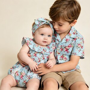 Puede incluir: Un beb&eacute; con un pelele floral azul claro y una diadema a juego es sostenido por un ni&ntilde;o que lleva una camisa floral azul claro y pantalones cortos color caqui. El pelele tiene un escote con volantes y ribete de encaje.
