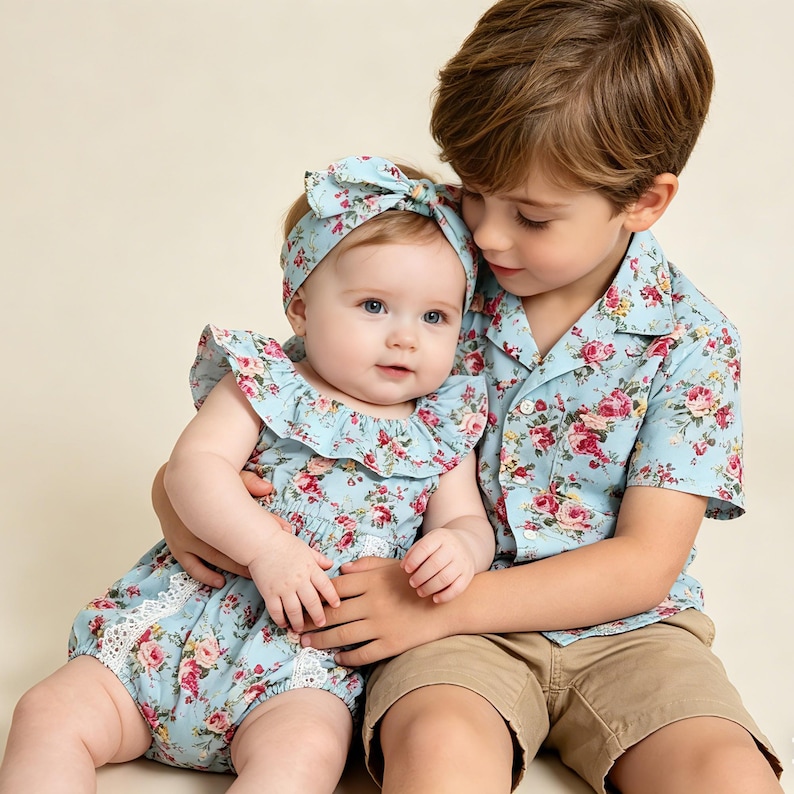 Puede incluir: Un beb&eacute; con un pelele floral azul claro y una diadema a juego es sostenido por un ni&ntilde;o que lleva una camisa floral azul claro y pantalones cortos color caqui. El pelele tiene un escote con volantes y ribete de encaje.
