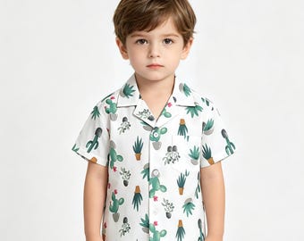 Puede incluir: Una camisa blanca de manga corta con un estampado de cactus y suculentas verdes. La camisa tiene un pequeño bolsillo en el pecho y está hecha de una tela ligera. La camisa está diseñada para niños.