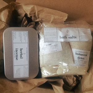 May include: A brown cardboard box containing a silver tin labelled "Herbal Incense" and a plastic bag with two white cloth pouches labelled "Herbal Bath Salts" and "Botanical Detox".