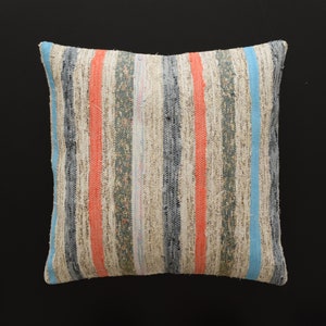 May include: A striped cushion with a cream background and blue, red, and green stripes. The cushion is made of a woven fabric and has a slightly distressed look.