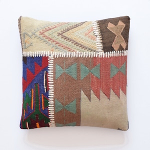 Può includere: Un cuscino patchwork con una varietà di motivi geometrici in tonalità di marrone, rosso, blu, verde e beige. Il cuscino è realizzato in tessuto tessuto e ha un bordo bianco cucito.