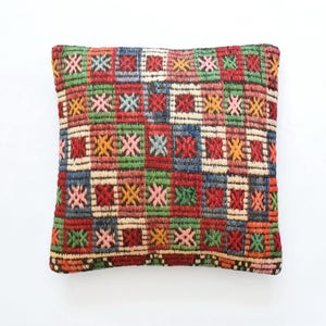 May include: A rectangular pillow with a colorful geometric pattern. The pillow is made of woven fabric and has a brown border. The pattern features squares and stars in shades of red, green, blue, yellow, and pink.