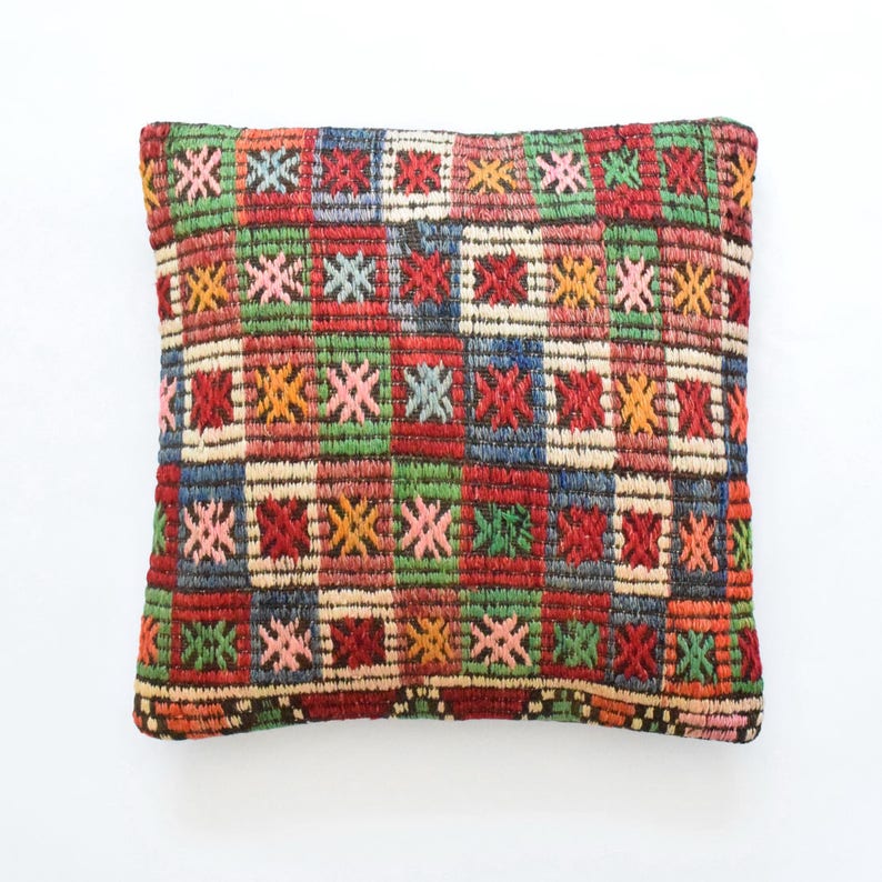 May include: A rectangular pillow with a colorful geometric pattern. The pillow is made of woven fabric and has a brown border. The pattern features squares and stars in shades of red, green, blue, yellow, and pink.