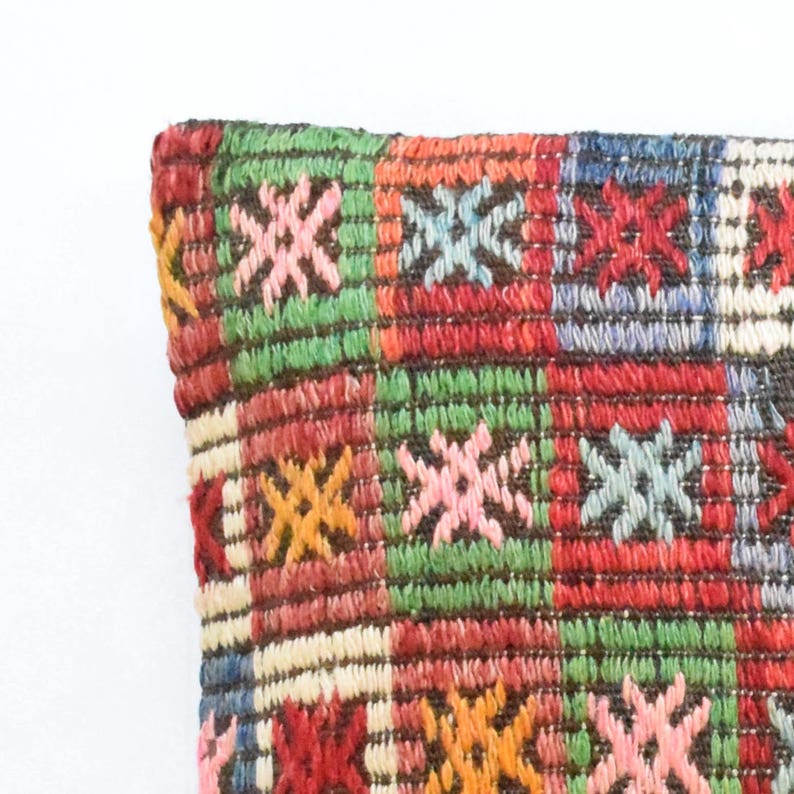 May include: A colorful pillow with a geometric pattern of red, green, blue, pink, orange, and white. The pillow is made of woven fabric and has a textured surface.