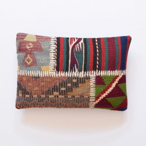 Può includere: Un cuscino rettangolare in patchwork con una varietà di colori e motivi, tra cui rosso, verde, blu e marrone. Il cuscino è realizzato in tessuto tessuto e ha una cucitura cucita attorno ai bordi.