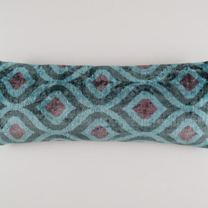 May include: A long, rectangular teal blue pillow with a geometric pattern of dark teal and burgundy diamonds. The pillow is made of a soft, plush fabric.