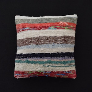 Può includere: Un cuscino a righe colorate con una trama tessuta. Il cuscino è realizzato in una varietà di colori, tra cui rosso, blu, verde e marrone.