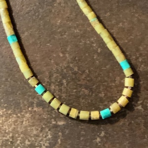 May include: A necklace made of yellow and turquoise beads. The beads are square shaped and strung together on a silver chain.