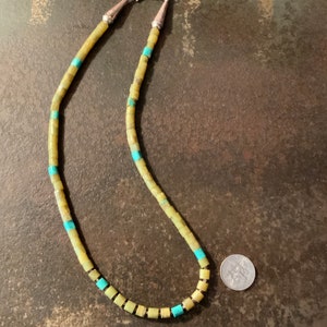 May include: A necklace made of light green and turquoise square beads with silver clasps. A US quarter is included for scale.