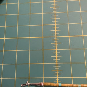 May include: A close-up of a turquoise and green beaded necklace with a silver clasp. The necklace is lying on a green cutting mat with white markings.