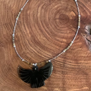 May include: A black onyx eagle pendant necklace with brown and silver beads. The eagle is carved in a detailed design with its wings spread.