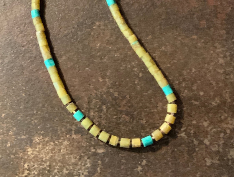 May include: A necklace made of yellow and turquoise beads. The beads are square shaped and strung together on a silver chain.