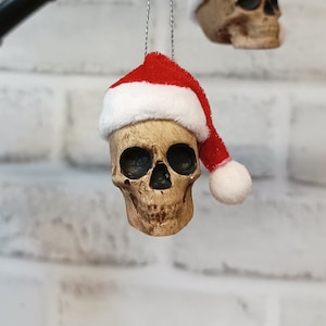 May include: Two white skull ornaments with red and white Santa hats hanging from a black branch.