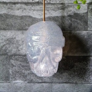 May include: A white glitter skull ornament hanging from a copper cord. The skull is translucent and has a sparkly finish.