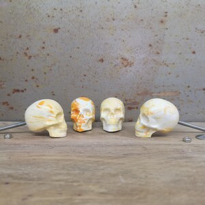 May include: Four white skull-shaped drawer pulls with yellow and orange marbling. The pulls are arranged in a row on a wooden surface.