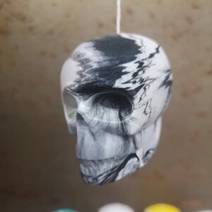May include: A white and black marbled skull ornament hanging from a white string. The skull is detailed with a black and white marbled design.
