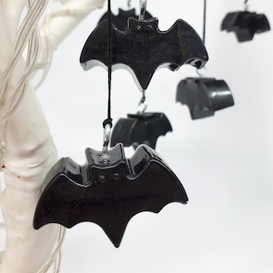 May include: A set of black bat-shaped ornaments hanging from a white branch. The bats are made of a shiny, smooth material and have a simple, classic design.