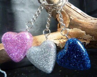 May include: Three heart-shaped keychains with glitter. The hearts are pink, silver, and blue.