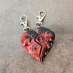 May include: A red and black heart-shaped keyring with a skull design. The keyring is made of two separate pieces that are connected by a metal ring.