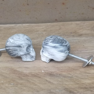 May include: Two black and white marbled skull drawer pulls with silver screws and metal backing plates.